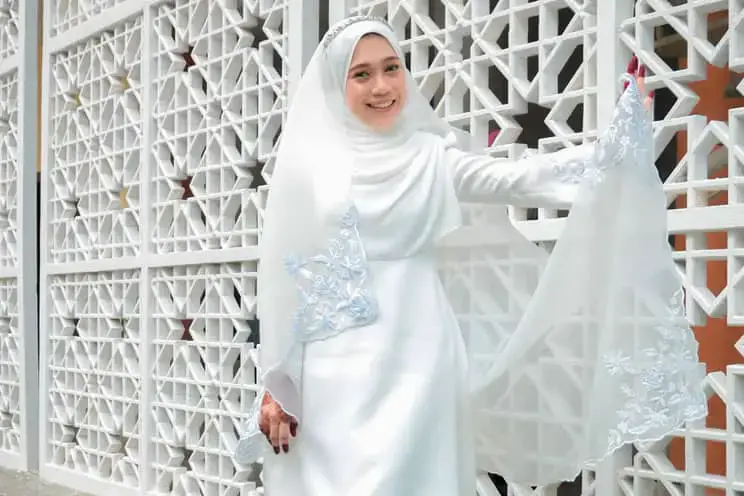 Muslim bride dress in white leaning against a wall